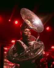 Student holding a tuba and standing on a stage with a backdrop of red lighting