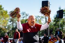 Older man in glasses cheering and holding pompoms in both hands during the Homecoming Parade