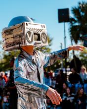 Student performer during the homecoming parade dressed in a metallic silver outfit with their face obscured by a boombox helmet